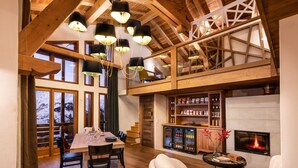 Una habitación amplia con techo alto, vigas de madera, chimenea y un área de comedor con mesa y sillas.
