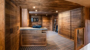 Interior de una cabaña de madera con piso a cuadros, un mostrador central y esquíes apoyados en la pared.