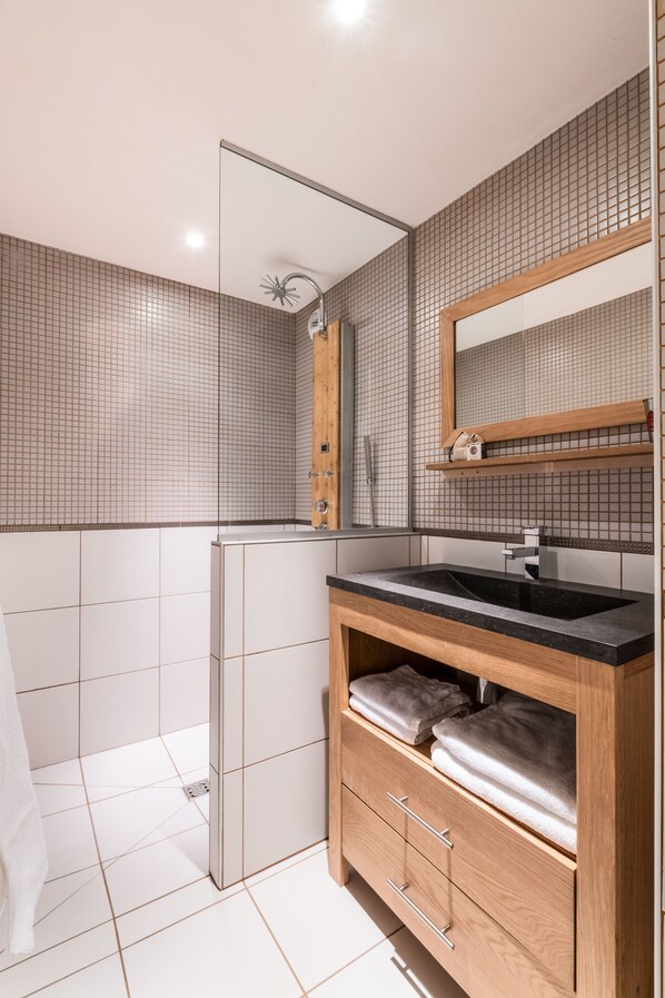 A modern bathroom with a large mirror, a black sink, and a shower enclosure.