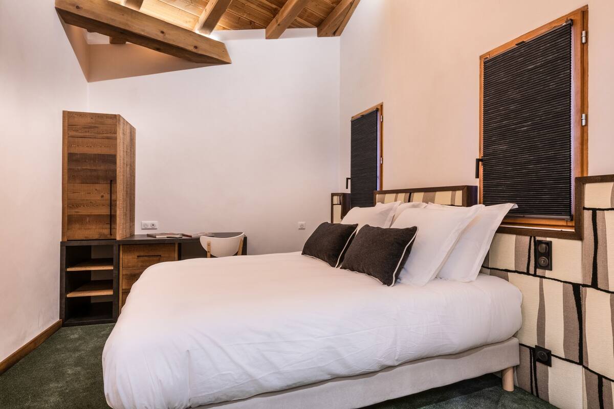 A bedroom with a large bed, wooden headboard, a bedside table, a chair, and a built-in wardrobe.