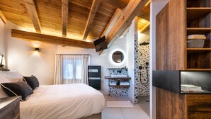 Un dormitorio con cama, televisión, baño con lavamanos y espejo, y vigas de madera en el techo.