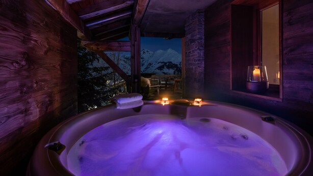 Una cabaña de madera con jacuzzi, velas y vistas a montañas nevadas.