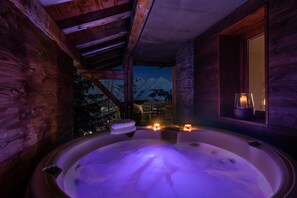 A wooden cabin with a hot tub, candles, and a view of snow-capped mountains.