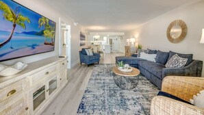 A living room with a TV, sofas, a coffee table, and a large painting. - Vacation Villas #233 Luxury Beachfront Condo (Fort Myers Beach)