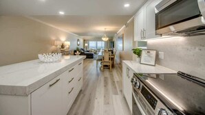 A modern kitchen with a large island, built-in oven, and a dining area with a view. - Vacation Villas #233 Luxury Beachfront Condo (Fort Myers Beach)