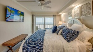 A hotel room with a bed, a ceiling fan, a large window with a view, and a painting on the wall. - Vacation Villas #233 Luxury Beachfront Condo (Fort Myers Beach)