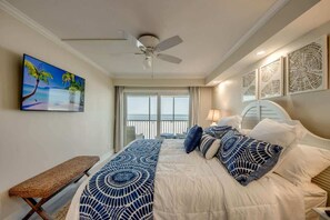 Una habitación de hotel con una cama, un ventilador de techo, un ventanal con vistas y un cuadro en la pared.