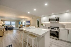 Una cocina moderna con armarios blancos, una isla central con taburetes, horno integrado y microondas.