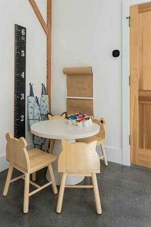 A room with a round table, four wooden chairs, a height chart, and a roll-up banner with 'Everybody is welcome' written on it.