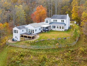 Una casa gran i blanca amb un porxo cobert i un pati tancat per una tanca, envoltada d'arbres de fullatge daurat.