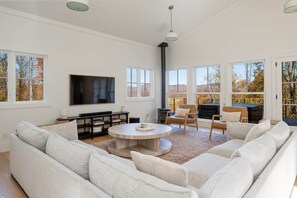 A spacious living room with a large sofa, a coffee table, and a fireplace. There are multiple windows providing views of the outdoors. - 8BR/13 bed Luxury Villa w/ Hot Tub (DT AVL 18min) (Fletcher)
