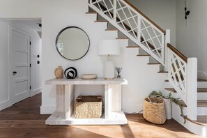 A staircase with white railings and wooden steps, a white console table with a mirror, a lamp, and decorative items, and a wicker basket on the floor. - 8BR/13 bed Luxury Villa w/ Hot Tub (DT AVL 18min) (Fletcher)