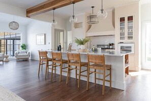 Een ruime keuken met een centraal eiland, houten stoelen, hanglampen en uitzicht op het buiten.