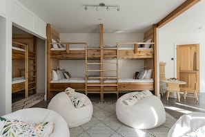 Une pièce avec des lits superposés, une échelle, des poufs, une petite table et une porte.