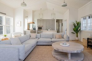 A spacious living room with a large L-shaped sectional sofa, a round coffee table, and a kitchen area with grey cabinets and a built-in oven. - 8BR/13 bed Luxury Villa w/ Hot Tub (DT AVL 18min) (Fletcher)