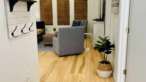 A narrow hallway with a wooden floor, a bed with striped bedding, a small table, and a potted plant. - Large, True 1 BR, Between Alys & Rosemary (Seacrest)