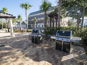 Un espace extérieur aménagé en terrasse, avec deux barbecues, une pergola et des palmiers.