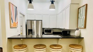 A kitchen with white cabinets, stainless steel appliances, a black countertop, and three wicker stools. - Large, True 1 BR, Between Alys & Rosemary (Seacrest)