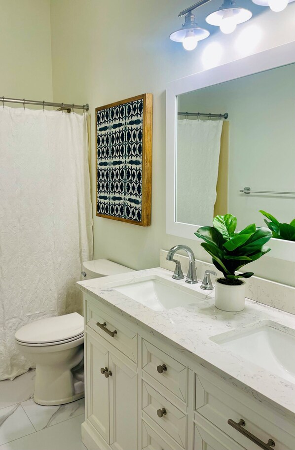 Une salle de bain avec des toilettes blanches, un lavabo doté d’un plan de travail en marbre, un miroir et une plante en pot.