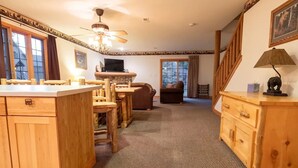 Une cuisine chaleureuse avec des meubles en bois, un coin repas avec des chaises, une cheminée et un escalier menant à un autre niveau.