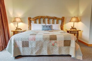 A neatly made bed with a quilt, two bedside lamps, and a wooden headboard.