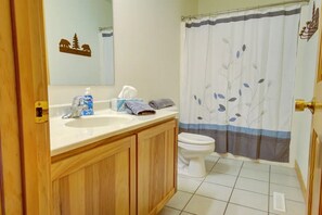 A bathroom with a wooden vanity, a white sink, a toilet, and a shower curtain with a floral pattern.