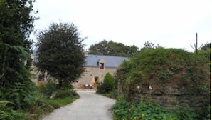 A gravel path leading to a stone building with a sloped roof, surrounded by greenery and a stone wall. - For a relaxing vacation in green surroundings (Pluvigner)