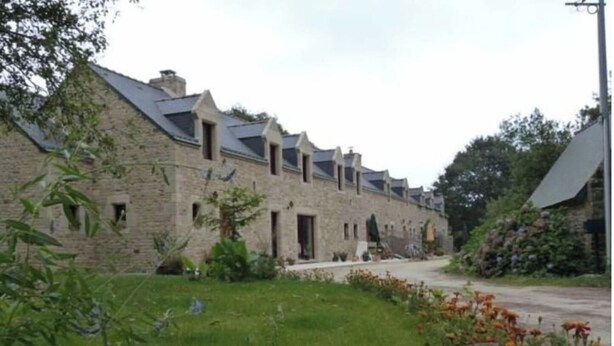 A row of stone buildings with multiple windows and a grassy area with flowers. - For a relaxing vacation in green surroundings (Pluvigner)
