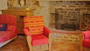 A cozy living room with a stone fireplace, a wooden sideboard, and two patterned armchairs. - For a relaxing vacation in green surroundings (Pluvigner)