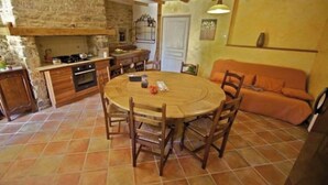 A cozy kitchen with a round wooden table and chairs, a stone wall, and a tiled floor. - For a relaxing vacation in green surroundings (Pluvigner)