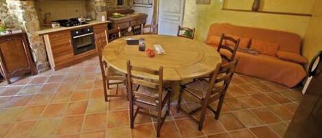 A cozy kitchen with a round wooden table and chairs, a stone wall, and a tiled floor.