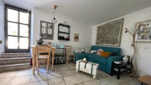 A living room with a teal sofa, a wooden dining table, a coffee table, and a staircase leading to an upper floor. - THE SECRET GARDEN (Forza d'Agrò)