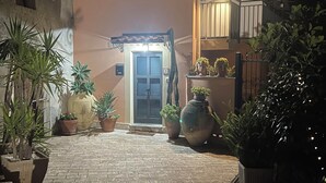 A paved courtyard with potted plants and a building entrance at night. - THE SECRET GARDEN (Forza d'Agrò)