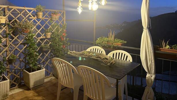 An outdoor patio with a table and chairs, surrounded by potted plants and a wooden lattice structure. - THE SECRET GARDEN (Forza d'Agrò)