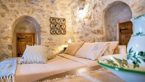 A stone-walled room with a bed, a wooden door, and a wall-mounted light fixture.