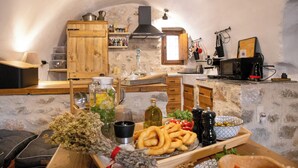 A rustic kitchen with stone walls, wooden cabinets, and a variety of kitchenware and food items on the counter.