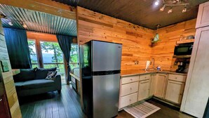A compact kitchen with wooden cabinetry, a refrigerator, and a dining area with a sofa.