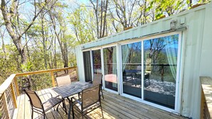 A deck with a table and chairs, a sliding glass door, and a view of trees.