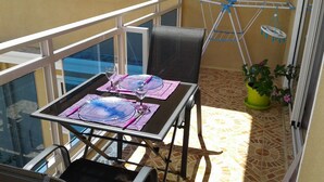Un balcón con una mesa preparada para dos, una silla, una planta en maceta y un tendedero.