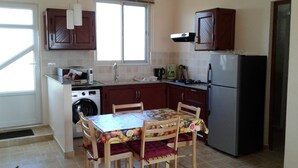 Una cocina compacta con lavadora, refrigerador, armarios de madera, una mesa de comedor con sillas y un ventanal.