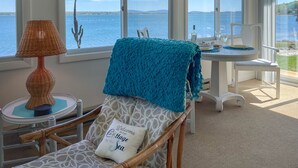 A cozy room with a view of the sea, featuring a wicker lamp, a chair with a cushion, and a table with a bottle and glasses. - Acadia Bay Cottages (Surry)