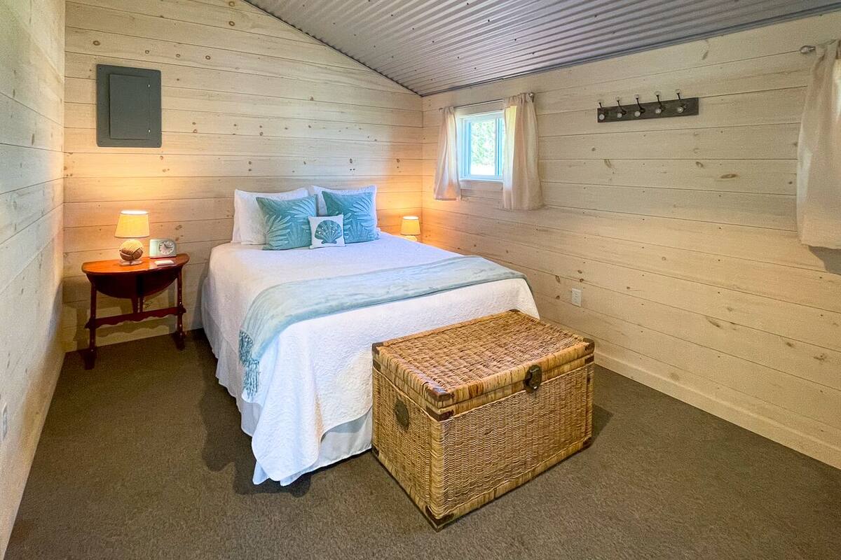 A cozy bedroom with a bed, bedside lamps, a wicker chest, and a window with curtains.