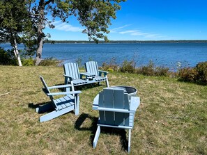 Järvenrantapaikka, jossa on Adirondack-tyylisiä puutarhatuoleja ja pöytä, ja ympäristönä on nurmikkoa ja puita.