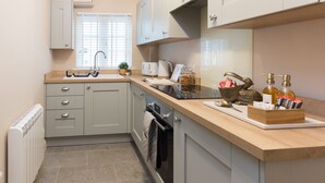 A modern kitchen with a built-in oven, a sink, and a countertop with various items including a coffee maker, a kettle, and a decorative bird. - Bridge Hideaway (Llangollen)