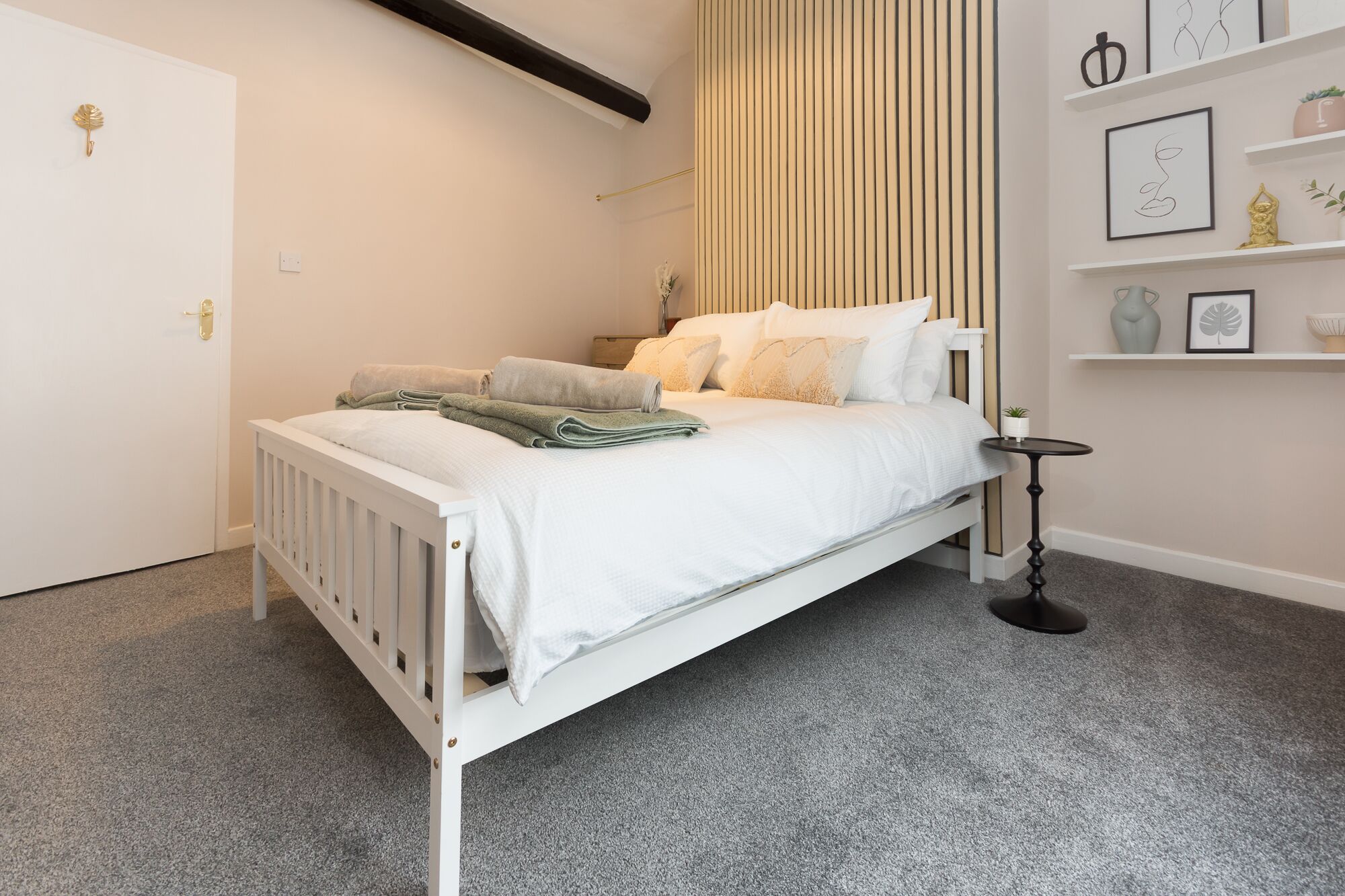 A neatly arranged bedroom with a white bed, a bedside table, and a wall-mounted shelf with decorative items.