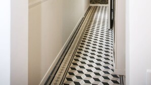 A narrow hallway with a patterned floor, a window with blinds, and a door with a light fixture. - Magnifique appartement familial grand boulevard-6P (Paris)