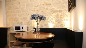 A cozy room with a stone wall, a round wooden table with a vase of flowers, a microwave, and a cushioned bench. - Magnifique appartement familial grand boulevard-6P (Paris)
