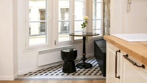 A kitchen with a window, a small round table, a black stool, and a white cabinet. - Magnifique appartement familial grand boulevard-6P (Paris)