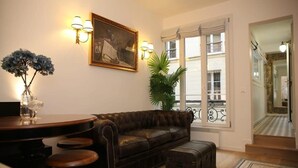 A living room with a dark brown leather sofa, a small round table with stools, a potted plant, and a painting on the wall. - Magnifique appartement familial grand boulevard-6P (Paris)