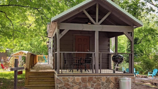 Une cabane en bois avec un porche, des fondations en pierre et un barbecue à l’extérieur.